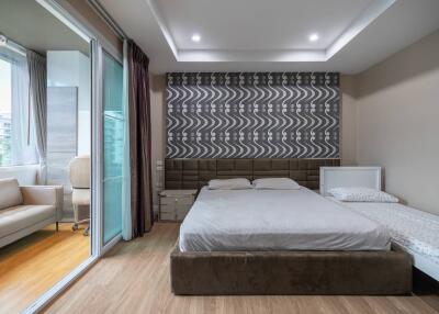 Modern bedroom with a large bed, a single bed, a unique patterned accent wall, and an adjacent sitting area with balcony access