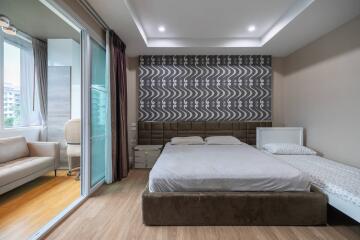 Modern bedroom with a large bed, a single bed, a unique patterned accent wall, and an adjacent sitting area with balcony access