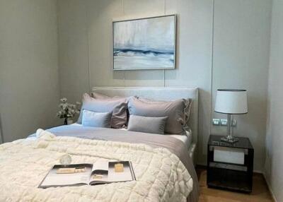 Cozy modern bedroom with neatly arranged bed, bedside table, lamp, and a painting on the wall