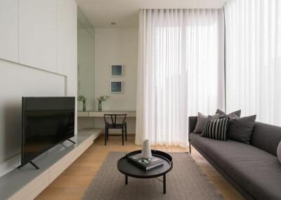 Modern living room with grey sofa, wall-mounted TV, and large windows with sheer curtains