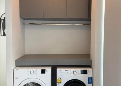 A compact laundry room with a washing machine and a dryer under a countertop, with storage cabinets above.