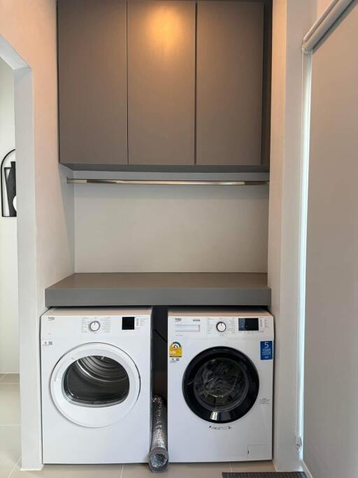 A compact laundry room with a washing machine and a dryer under a countertop, with storage cabinets above.