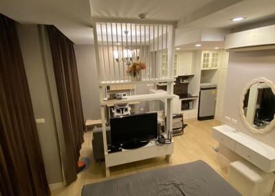 Interior view of a studio apartment with bed, TV, partition, kitchen area, and vanity table