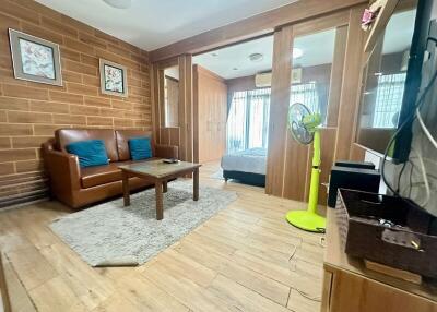 Living area with wooden floor, brick accent wall, and adjacent bedroom