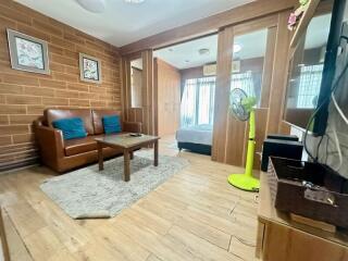 Living area with wooden floor, brick accent wall, and adjacent bedroom