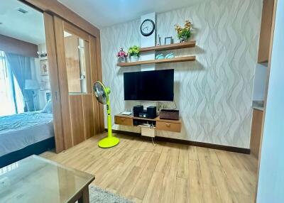 Living room with TV, shelves, and a view into the bedroom