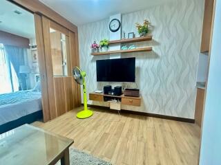 Living room with TV, shelves, and a view into the bedroom