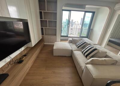 Modern living room with a large window offering a city view, furnished with a beige sofa and built-in shelving unit.