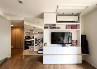 Modern living room with wooden flooring, built-in entertainment unit, and large mirror.