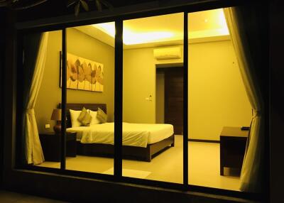 A well-lit bedroom with a large bed, two bedside tables with lamps, a piece of wall art, air conditioning, and a wooden door