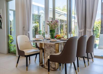 Modern dining room with glass table, cushioned chairs, and garden view