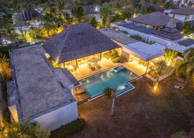 Aerial view of a modern villa with a swimming pool, surrounded by lush greenery, at dusk.