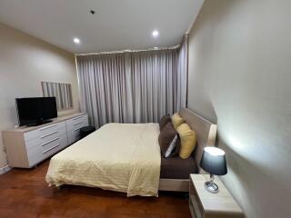 Spacious bedroom with a bed, dresser, TV, and nightstand with lamp