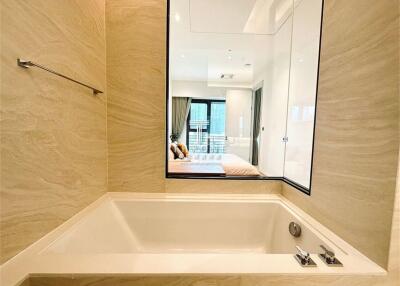 Modern bathroom with a bathtub and a large mirror reflecting a bedroom
