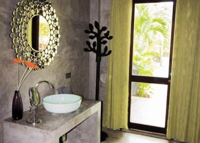 Modern bathroom with a large vanity mirror, round sink, decorative vase, and a towel tree near the window.