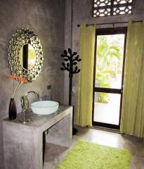 Modern bathroom with a large vanity mirror, round sink, decorative vase, and a towel tree near the window.