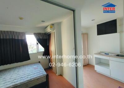 A bedroom with an attached kitchenette area featuring a bed, a window, an air conditioning unit, and kitchen cabinets.