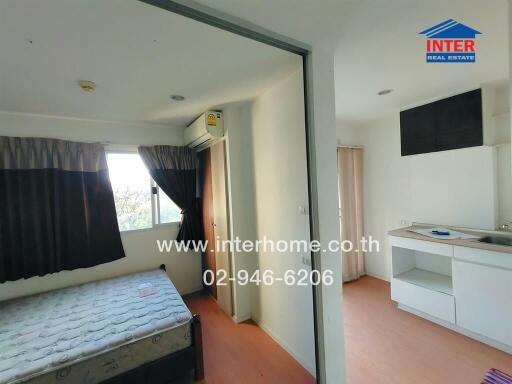 A bedroom with an attached kitchenette area featuring a bed, a window, an air conditioning unit, and kitchen cabinets.