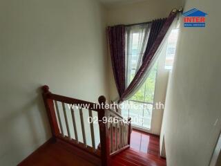 Staircase with wooden railing and window with curtains