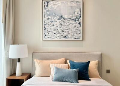 Modern bedroom with a neatly made bed, side table, lamp, and abstract wall art