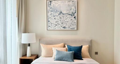 Modern bedroom with a neatly made bed, side table, lamp, and abstract wall art