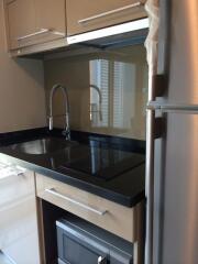 Modern compact kitchen with sleek cabinetry, black countertop, built-in cooktop, and stainless steel refrigerator