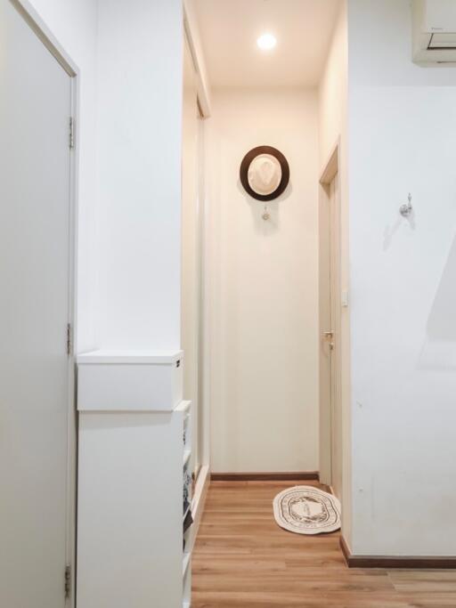 A narrow hallway with a wooden floor, white walls, and a hat hung on the wall