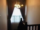 Staircase with chandelier and curtained window