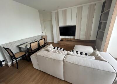 Modern living room with sofa, wall-mounted TV, and dining area