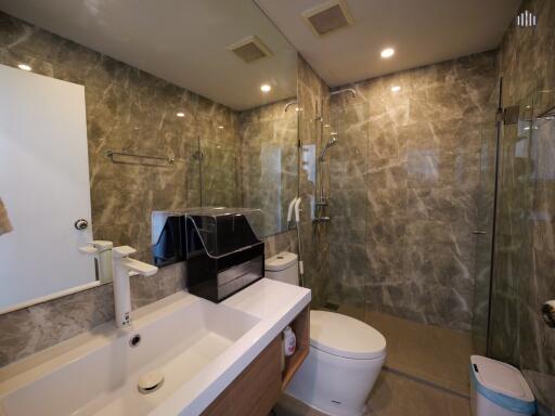 Modern bathroom with marble walls, glass shower, and white fixtures