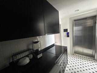 Modern kitchen with black cabinetry, tiled floor, and access to elevator