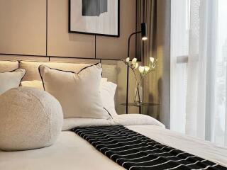 Modern bedroom with cozy bed, decorative pillows, and bedside table with a lamp and flowers