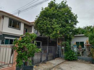 Front view of a multi-story residential building with a gate and lush greenery