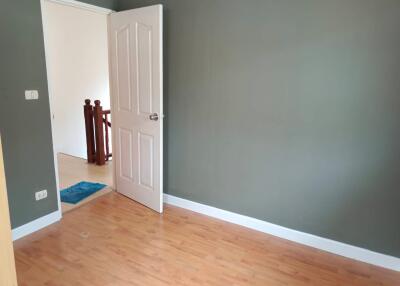 Empty bedroom with wooden flooring and an open door leading to a hallway.