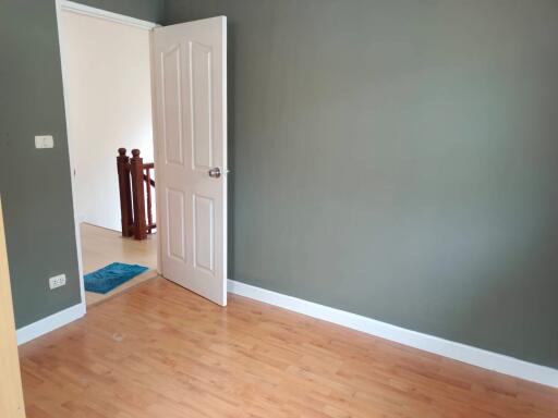 Empty bedroom with wooden flooring and an open door leading to a hallway.