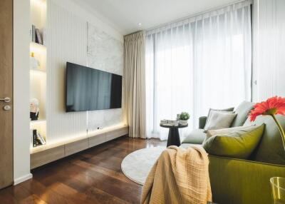 Modern living room with wall-mounted TV, large window, and comfortable green sofa