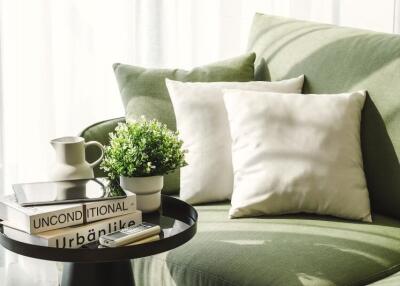 Cozy living room corner with green sofa, white pillows, potted plant, and decorative books.