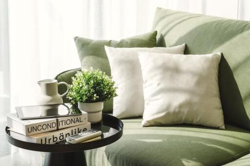 Cozy living room corner with green sofa, white pillows, potted plant, and decorative books.