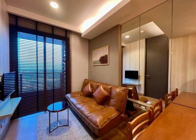 Modern living room with brown leather sofa, TV, and large window with blinds