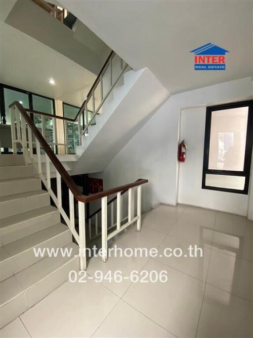 Staircase area with tiled floor and railing, adjacent to a glass-paneled wall and corridor