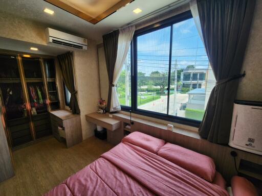 Bedroom with large window, bed with pink sheets, air conditioning, and wardrobe