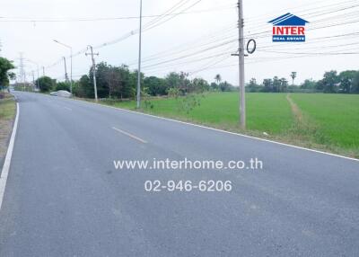 Road near a property with a green field and advertisement for real estate