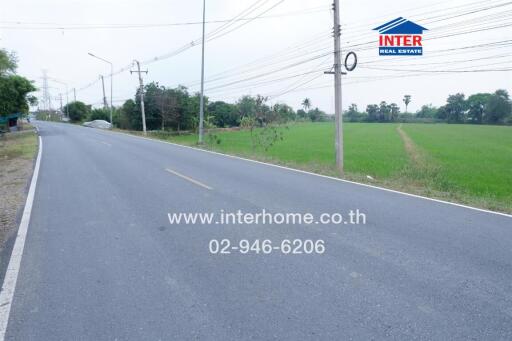 Road near a property with a green field and advertisement for real estate