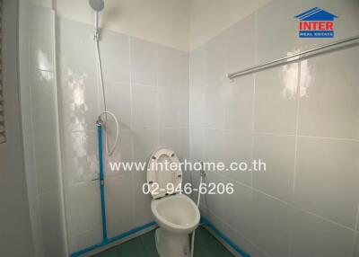 Photo of a clean white-tiled bathroom with a toilet, showerhead, and towel rail