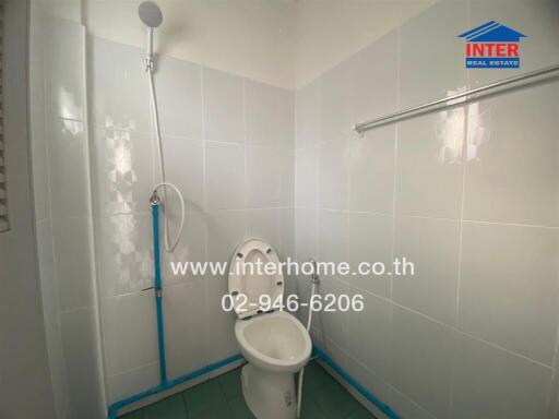 Photo of a clean white-tiled bathroom with a toilet, showerhead, and towel rail