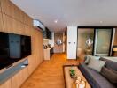 Modern living area with open kitchen, television, couch, and access to bedroom and bathroom