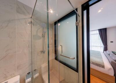 Modern bathroom with a glass-enclosed shower adjacent to a bedroom
