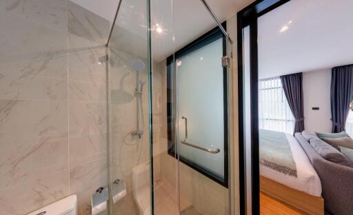 Modern bathroom with a glass-enclosed shower adjacent to a bedroom