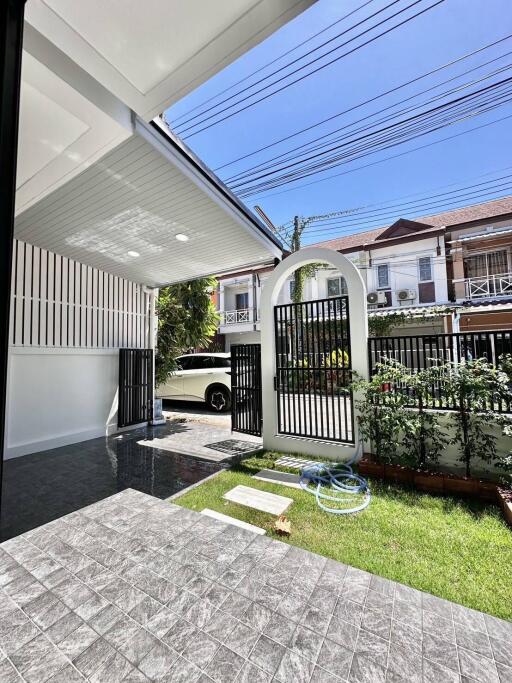 Covered patio leading to a garden area with a gate view of residential buildings