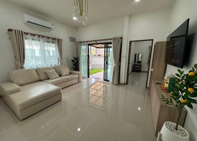 Modern living room with beige sofa, air conditioner, TV, and sliding glass door leading outside.